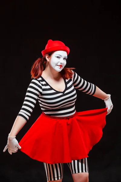 Portret van vrouwelijke mime artiest optredend, geïsoleerd op zwarte achtergrond. vrouw in gestreepte kleren houden haar rode rok en glimlachen — Stockfoto