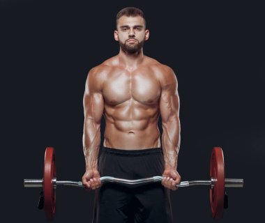 Siyah arka planda izole edilmiş halterle egzersiz yapan güçlü bir vücut geliştiricinin ön görüntüsü.