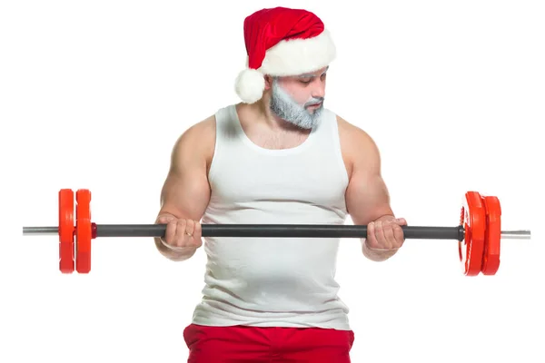 Navidad. Santa Claus musculoso fuerte con la barba gris que usa el sombrero de Navidad y los pantalones cortos rojos está levantando una barra pesada en un gimnasio que realiza un entrenamiento aislado en fondo blanco — Foto de Stock