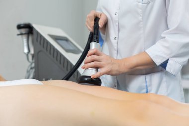 İnce bir kadın, ultrason etkisiyle yağ hücrelerini ayırmak için güzellik salonunda sıkı kalçalarına anti-selülit ve anti-yağ terapisi uygular.