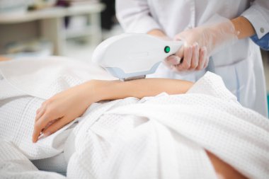 Modern bir kozmetoloji ofisinde profesyonel bir uzman tarafından genç bir kızın kolunda lazer kılı alınması.