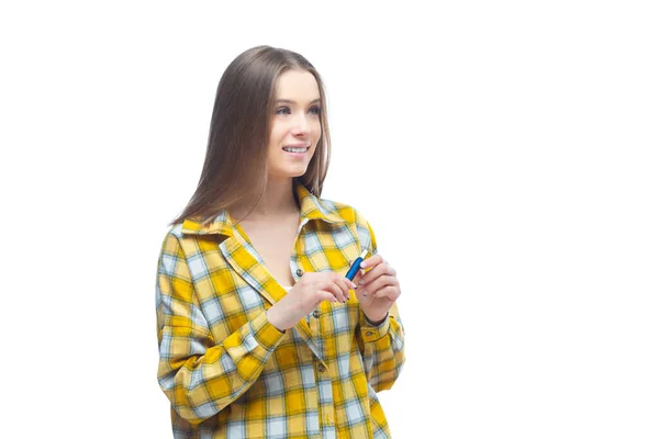 Портрет молодої жінки в жовтій картатій сорочці, яка дивиться на електронну сигарету в руках ізольовано на білому тлі — стокове фото
