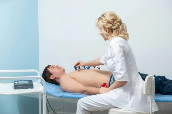 Egy kardiológus orvos érzékelőket alkalmaz egy férfi meztelen testén, aki egy kórházi elektrokardiográfiás eljárás során fekszik a kanapén. — Stock Fotó