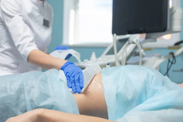 Foto de un médico limpiando el gel médico de un abdomen de una mujer embarazada con una servilleta después del diagnóstico por ultrasonido del feto durante una cita programada —  Fotos de Stock