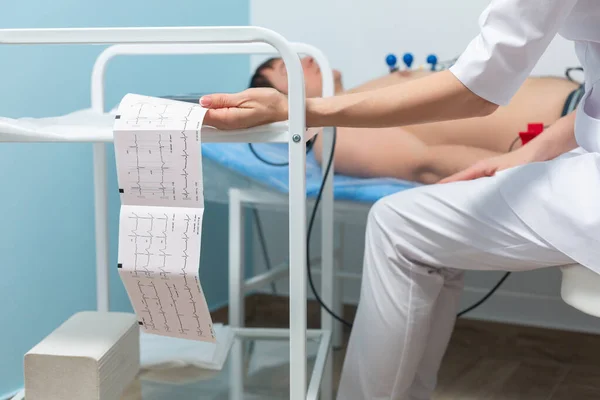 Foto de perto de um eletrocardiógrafo imprimindo os resultados de um cardiograma durante uma consulta médica na clínica — Fotografia de Stock