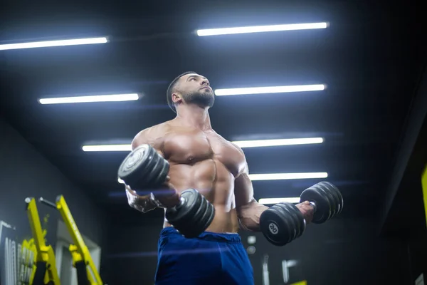 Blick von unten auf einen starken Athleten, der im Fitnessstudio Hanteln hebt — Stockfoto