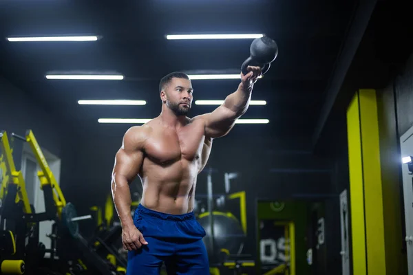 Portrait of a muscular sportsman performing kettlebell swings with one hand in a gym — Stock Photo, Image