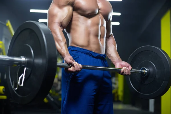 Close up of a naked muscular torso and strong man arms lifting a heavy barbell while training in a gym — 图库照片