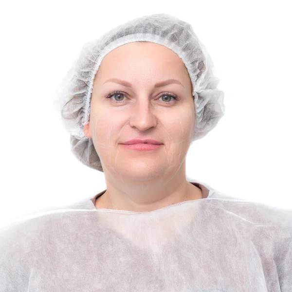 Full-face portrait of a happy woman patient of a cosmetology office in a medical cap standing with marks on her face with a white cosmetic pencil before the rejuvenation and facelift procedure — Stock Photo, Image
