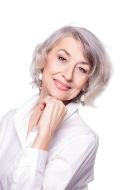 Güzel gri saçlı orta yaşlı kadının portresini yakından çek. Çenesini yumruğa yaslamış, geniş bir gülümsemeyle kameraya bakıyor ve beyaz stüdyo arka planında izole edilmiş mutluluğu gösteriyor.
