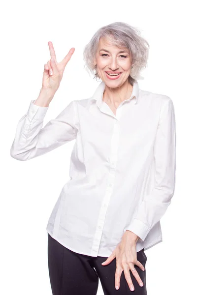 Senior grey-haired woman wearing elegant shirt standing over isolated white background smiling with happy face doing victory sign — Fotografia de Stock
