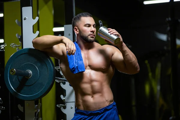 Jonge sexy sportman is ontspannen na een harde training in een fitnessruimte in de buurt van een lange halter met een handdoek en drinkwater — Stockfoto