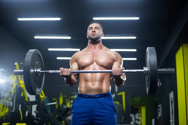 Nahaufnahme eines starken muskulösen Athleten, der eine schwere Langhantel hebt und seine Muskeln in einem Fitnessstudio zeigt — Stockfoto