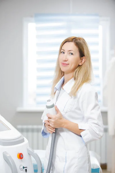 Nette Ärztin steht in einem modern ausgestatteten Schönheitssalon und hält ein RF-Hebegerät in der Hand, das bereit ist, Patienten aufzunehmen — Stockfoto