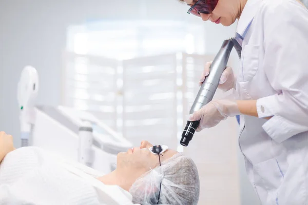 Vista lateral de la cara de una joven con gafas protectoras durante un procedimiento de pelado de carbono en un salón de belleza — Foto de Stock