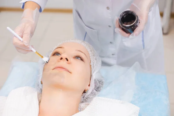 Ręce specjalisty kosmetologii stosującego nanogel węglowy na twarz młodej pacjentki za pomocą pędzla, przygotowującego się do zabiegów obierania węgla — Zdjęcie stockowe
