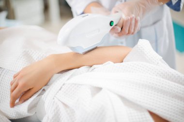 Modern bir kozmetoloji ofisinde profesyonel bir uzman tarafından genç bir kızın kolunda lazer kılı alınması.