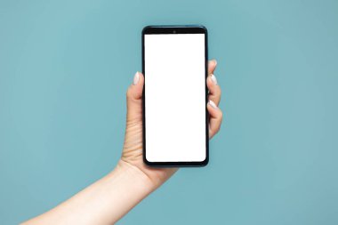 Mavi arka planda beyaz bir reklam ekranı olan akıllı telefonlu bir kadın elinin yakın çekimi. Yapıştırıcı kopyala.