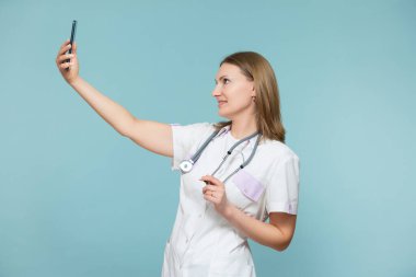 Akıllı telefonlu bir kadın doktor mavi arka planda selfie çeker. Kopyala yapıştır. sağlık hizmeti kavramı.