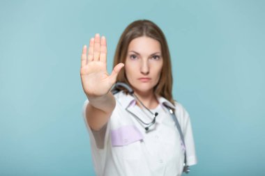 Steteskoplu güzel bir bayan doktor, mavi arka planda, elinde dur işareti var. Kopyala yapıştır. Sağlık hizmeti konsepti. Hastalığı durduralım..