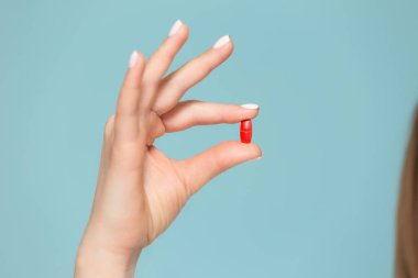 Mavi arka planda kırmızı haplı bir elin yakın çekimi. Kopyala yapıştır. Uyuşturucu saklama kavramı.