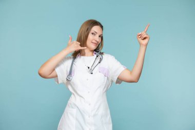 Bir kadın doktor bir telefon sembolü gösterir ve mavi arka planda bir reklam yöntemi ya da telefon numarasına işaret eder. Kopyala yapıştır. sağlık hizmeti kavramı.