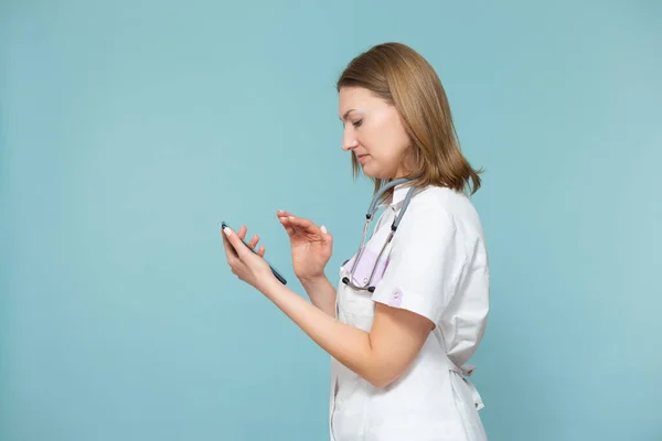 Un medico donna con uno smartphone conduce una consultazione online, supporta il paziente per telefono, su uno sfondo blu. Copia incolla. Concetto sanitario a distanza. — Foto Stock