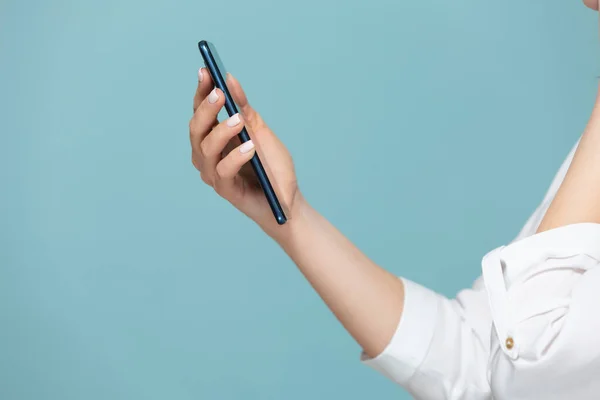 Κοντινό πλάνο μιας γυναίκας χέρι με ένα smartphone στο οποίο υπάρχει μια λευκή οθόνη για τη διαφήμιση, σε μπλε φόντο. Αντιγραφή επικόλλησης. — Φωτογραφία Αρχείου