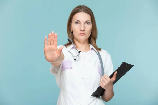 Bella donna medico con uno stetoscopio e una tavoletta nera, mostra un segno di stop con la mano, su uno sfondo blu. Copia incolla. concetto di assistenza sanitaria. Fermiamo la malattia. — Foto Stock