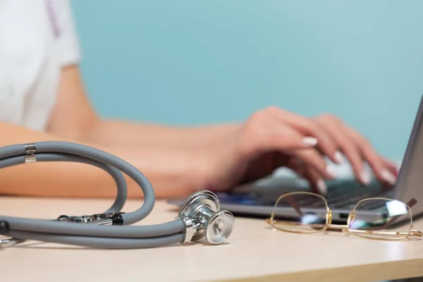 Eine Ärztin sitzt an einem Tisch und arbeitet an einem Laptop auf blauem Hintergrund. Copy paste. Gesundheitskonzept. — Stockfoto