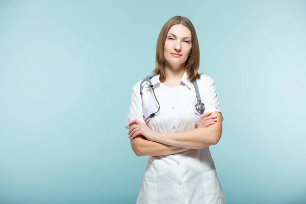 Piękna lekarka ze stetoskopem ze skrzyżowanymi ramionami na niebieskim tle. koncepcja opieki zdrowotnej. — Zdjęcie stockowe