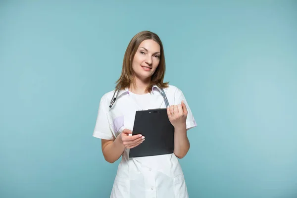 Hermosa doctora con un estetoscopio y una tableta negra, sobre un fondo azul. Copiar pasta. concepto de salud. — Foto de Stock