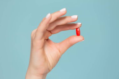 Mavi arka planda kırmızı haplı bir elin yakın çekimi. Kopyala yapıştır. Uyuşturucu saklama kavramı.