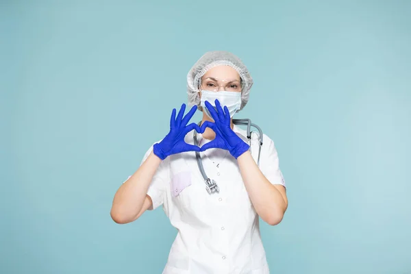 Símbolo del corazón, amor. Médico o enfermera con traje de protección personal con estetoscopio, sobre fondo azul. En una máscara, guantes, gafas y un sombrero. Copiar pasta. concepto de salud. —  Fotos de Stock