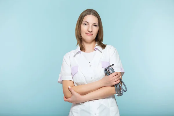 Hermosa doctora con un estetoscopio con brazos cruzados sobre un fondo azul. concepto de salud. —  Fotos de Stock