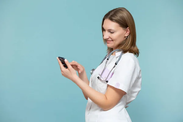 En kvinnlig läkare med en smartphone genomför en online konsultation, stöder patienten via telefon, på en blå bakgrund. Kopiera pastan. Distansvård. — Stockfoto