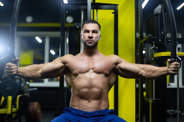 Attractive bodybuilder is working out in a gym training his chest muscles using sports equipment — Stock Photo, Image