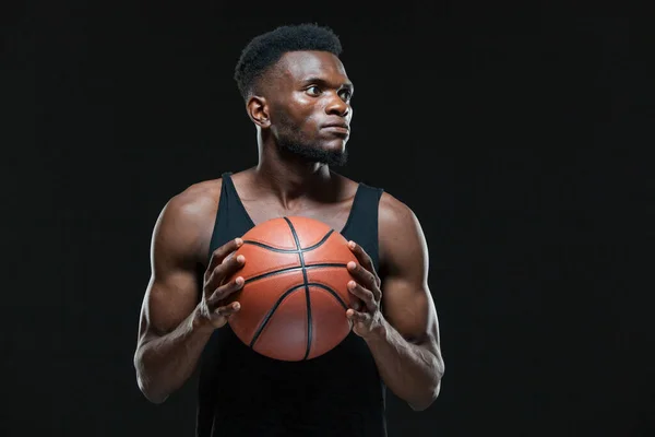 Siyah arka planda topla oynayan Afro-Amerikan erkek basketbolcunun portresi. Spor giyim bölümünde elinde basketbol topu tutan zinde bir genç. — Stok fotoğraf