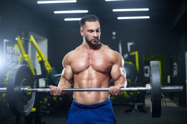 Güçlü, halterini kaldıran, spor salonunda kaslarını gösteren güçlü bir sporcunun yakın görüntüsü.