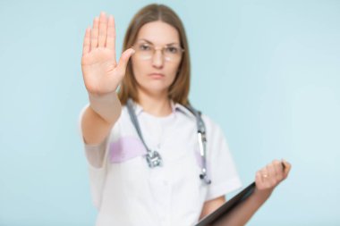 Steteskoplu ve siyah tabletli güzel bir kadın doktor mavi arka planda dur işareti gösteriyor. Kopyala yapıştır. Sağlık hizmeti konsepti. Hastalığı durduralım..