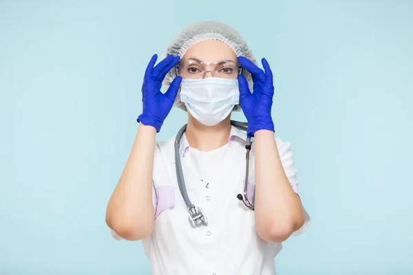 Médico o enfermera con traje de protección personal con estetoscopio, sobre fondo azul. En una máscara, guantes, gafas y un sombrero. Copiar pasta. concepto de salud. —  Fotos de Stock