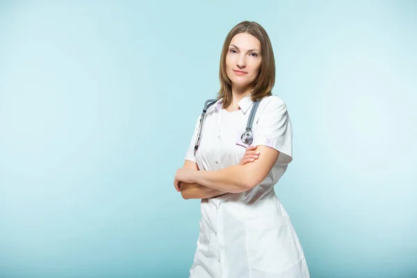 Médica bonita com um estetoscópio com braços cruzados em um fundo azul. conceito de saúde. — Fotografia de Stock