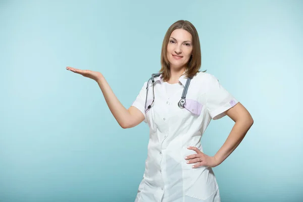 En vacker kvinnlig läkare med stetoskop pekar på den plats där det kommer att finnas viktig information, på en blå bakgrund. Kopiera pastan. hälso- och sjukvård. — Stockfoto