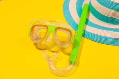 Sarı arka planda plaj aksesuarları, çizgili mavi şapka ve dalış maskesi. Plaj tatili kavramı, deniz turu, sıcak güneşli yaz. Reklam alanı