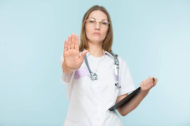 Steteskoplu ve siyah tabletli güzel bir kadın doktor mavi arka planda dur işareti gösteriyor. Kopyala yapıştır. Sağlık hizmeti konsepti. Hastalığı durduralım..