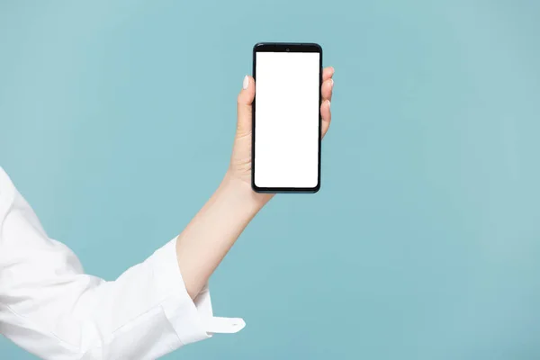 Großaufnahme einer Frauenhand mit einem Smartphone, auf dem ein weißer Bildschirm für Werbung auf blauem Hintergrund ist. Kopierpaste. — Stockfoto