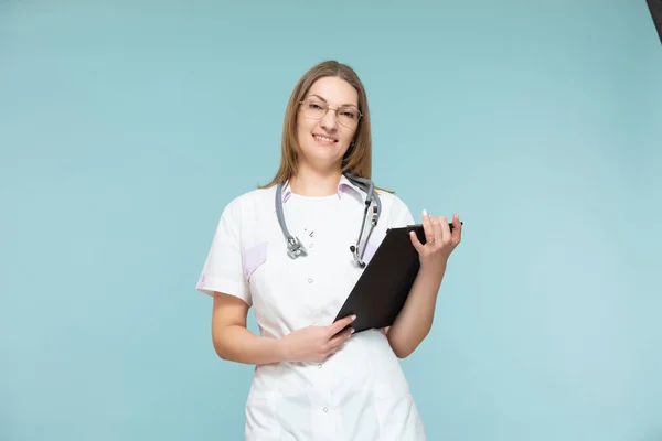 Hermosa doctora con un estetoscopio y una tableta negra, sobre un fondo azul. Copiar pasta. concepto de salud. — Foto de Stock