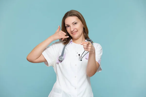 Kobieta lekarz pokazuje symbol telefonu i jej ręka wskazuje na sposób reklamy lub numer telefonu, na niebieskim tle. Skopiuj pastę. koncepcja opieki zdrowotnej. — Zdjęcie stockowe