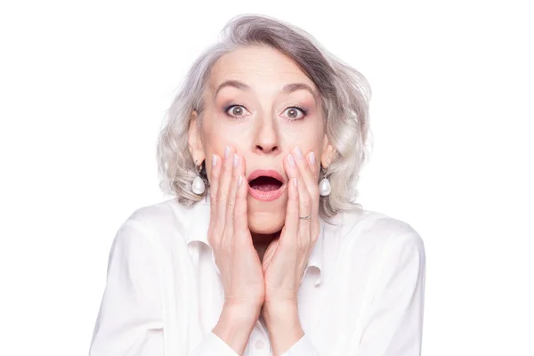 Portrait d'une femme mûre moderne regardant la caméra avec la bouche ouverte et les mains à son visage effrayé, surpris et choqué isolé sur fond blanc Images De Stock Libres De Droits