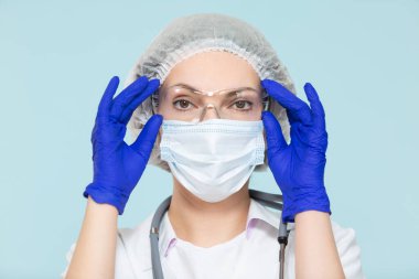 Mavi arka planda steteskoplu, koruyucu kıyafetli bir doktor ya da hemşire. Maskeli, eldivenli, gözlüklü ve şapkalı. Kopyala yapıştır. sağlık hizmeti kavramı.